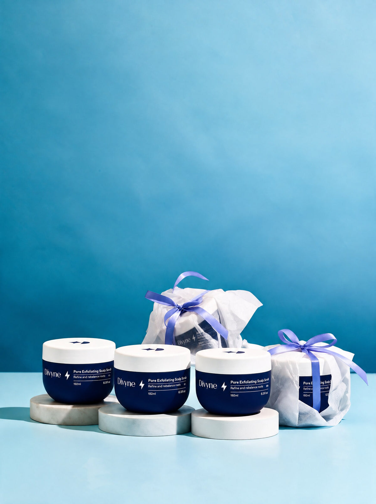 Scalp Scrub สามกระปุก กับอีกสองกระปุกห่อเป็นของขวัญ บนพื้นสีฟ้า